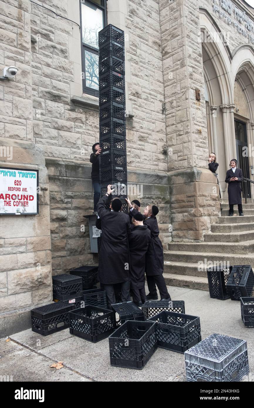 Ultra orthodox Jewish yeshiva students at an urban school build a tower out of milk crates during their recess. In New York City. Stock Photo