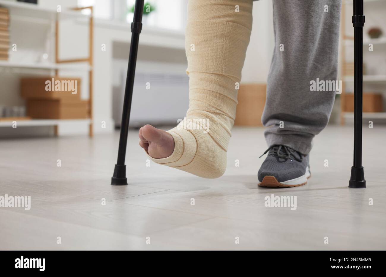 Close up of the feet of a young man with a broken leg walking with crutches at home Stock Photo