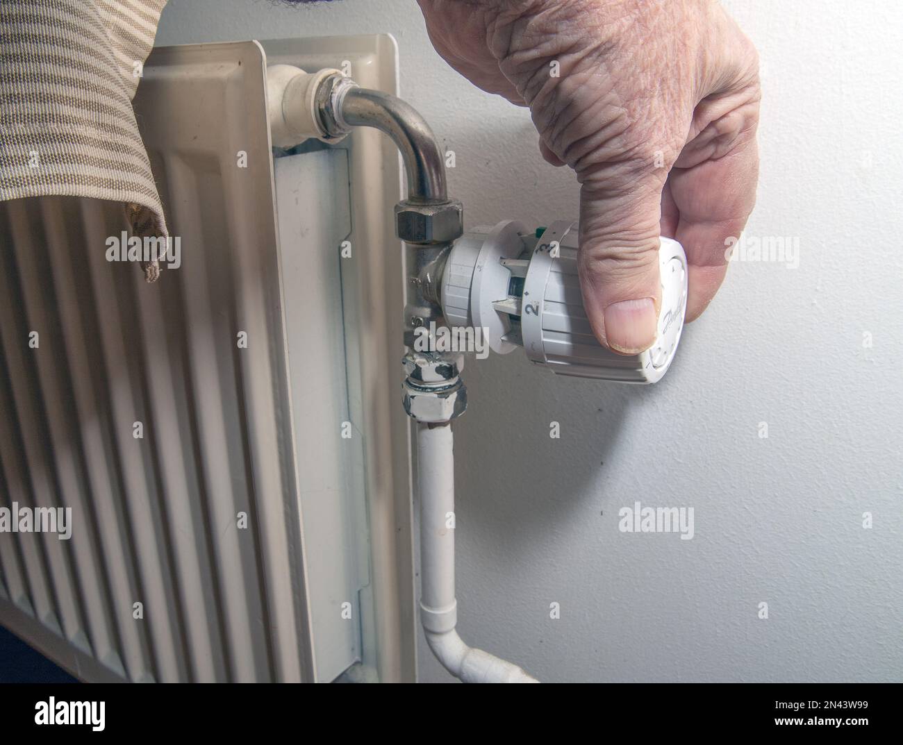 Closeup of person's hand using radiator thermostat, radiator and