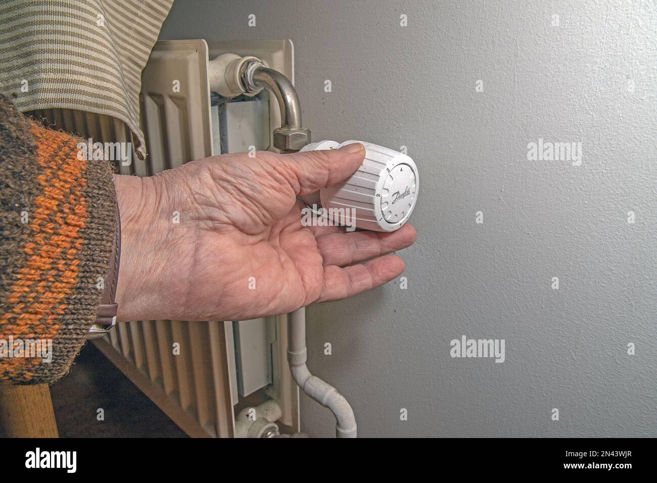 Close-up of person's hand using radiator thermostat, radiator and thermostat in flat - heater Stock Photo