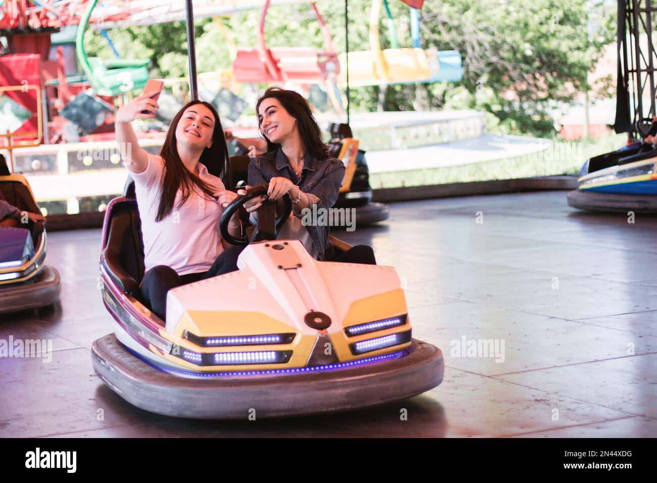 Two young women on a fun bumper car ride at the amusement park, taking ...