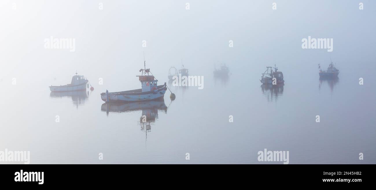 Boats Moored on River Ore off Orford Quay in Suffolk on a Cold February Morning as Fog & Mist Start to Clear Stock Photo