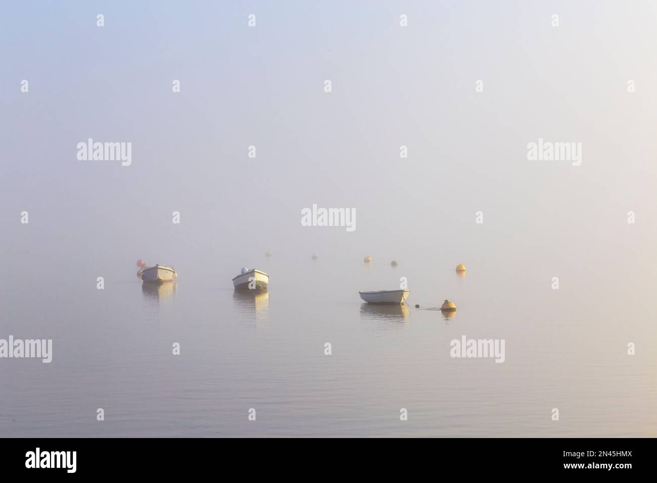 Dinghies Moored on River Ore off Orford Quay in Suffolk on a Cold February Morning as Fog & Mist Start to Clear with Yellow Mooring Buoys Stock Photo