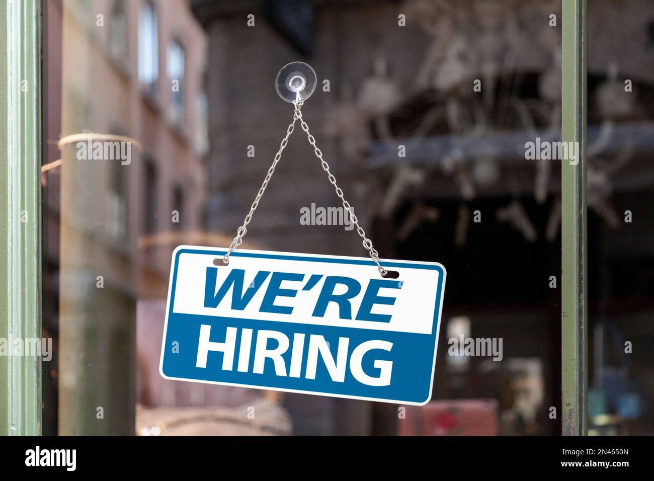 Close-up on a blue and white sign in a window with written in 'We're hiring'. Stock Photo