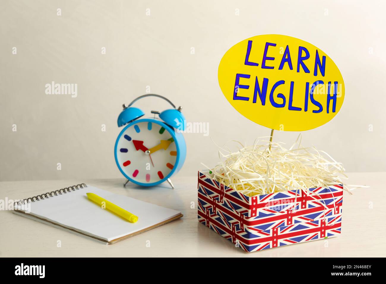 Notepad, alarm clock and sign with phrase Learn English in box on white