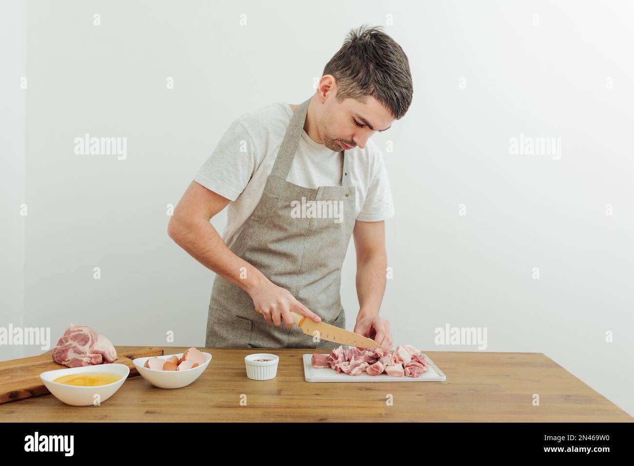 Premium Photo  Man cuts of fresh piece of meat on a wooden cutting board  in the home kitchen. a man in a striped apron with a big knife in his hands
