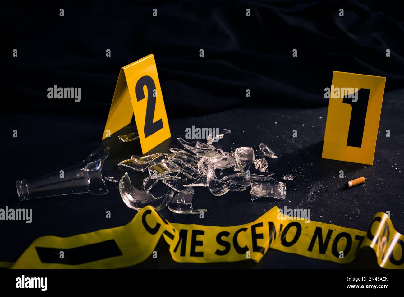 Broken bottle, yellow tape and evidence markers on black slate table