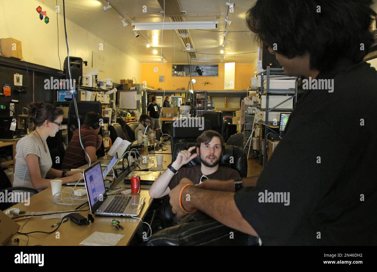 People talk and work on computers at a communal workbench at HeatSync ...