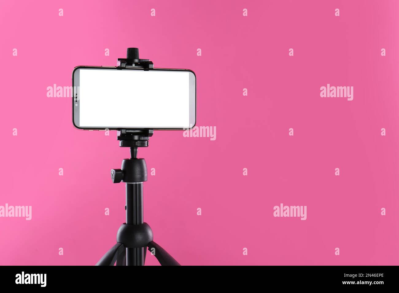 Smartphone with blank screen fixed to tripod on pink background. Space for text Stock Photo