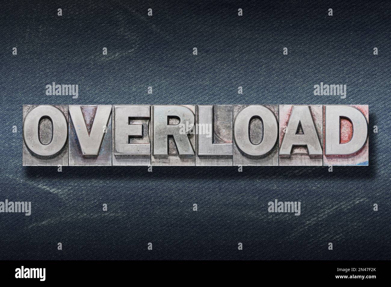 overload word made from metallic letterpress on dark jeans background Stock Photo