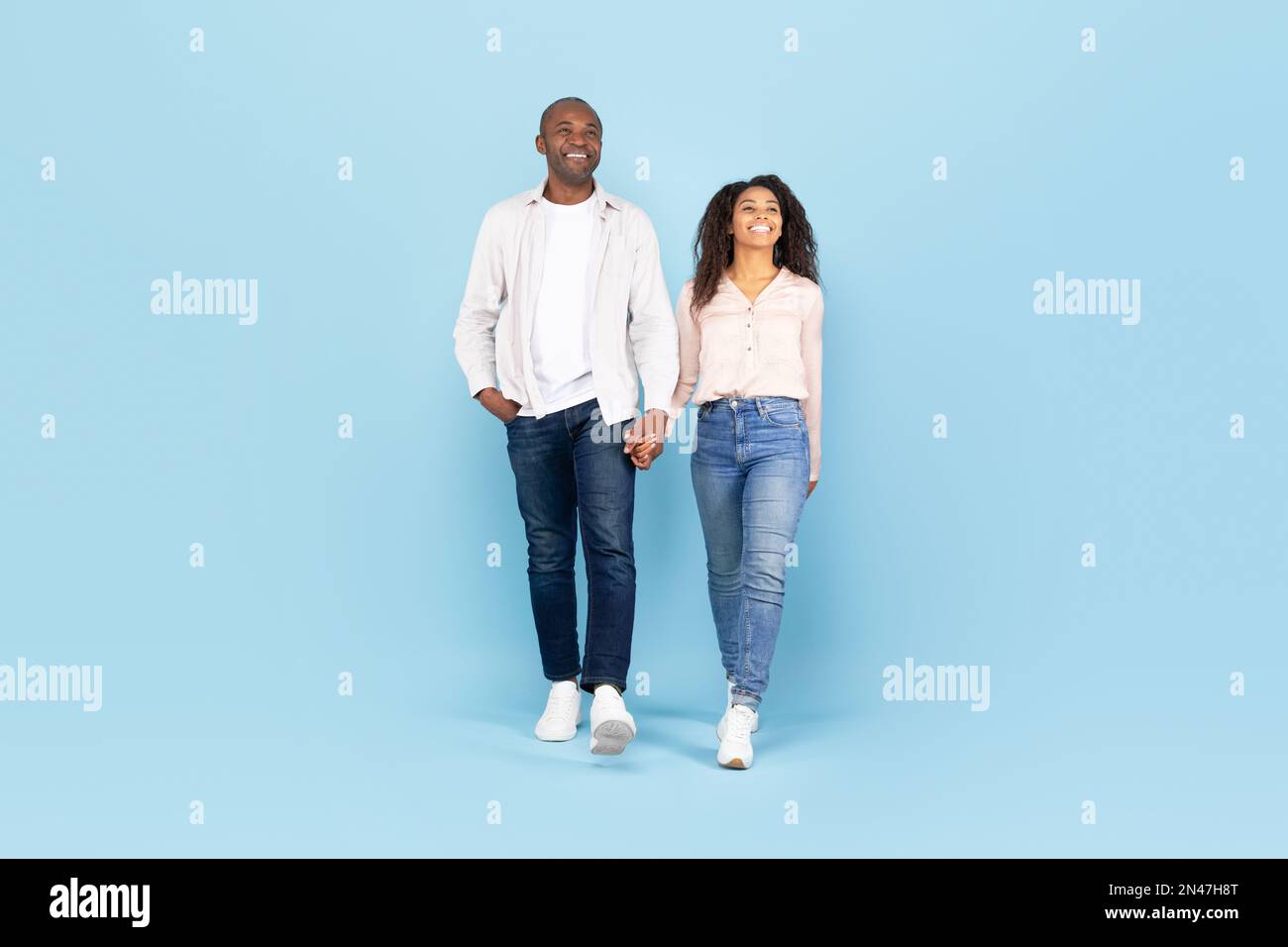 Happy african american couple walking, holding hands and looking away ...