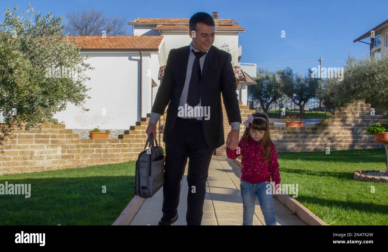 Image of a stylish businessman walking back from work on his driveway holding the hand of an adorable little girl. Love and acceptance of the daughter Stock Photo