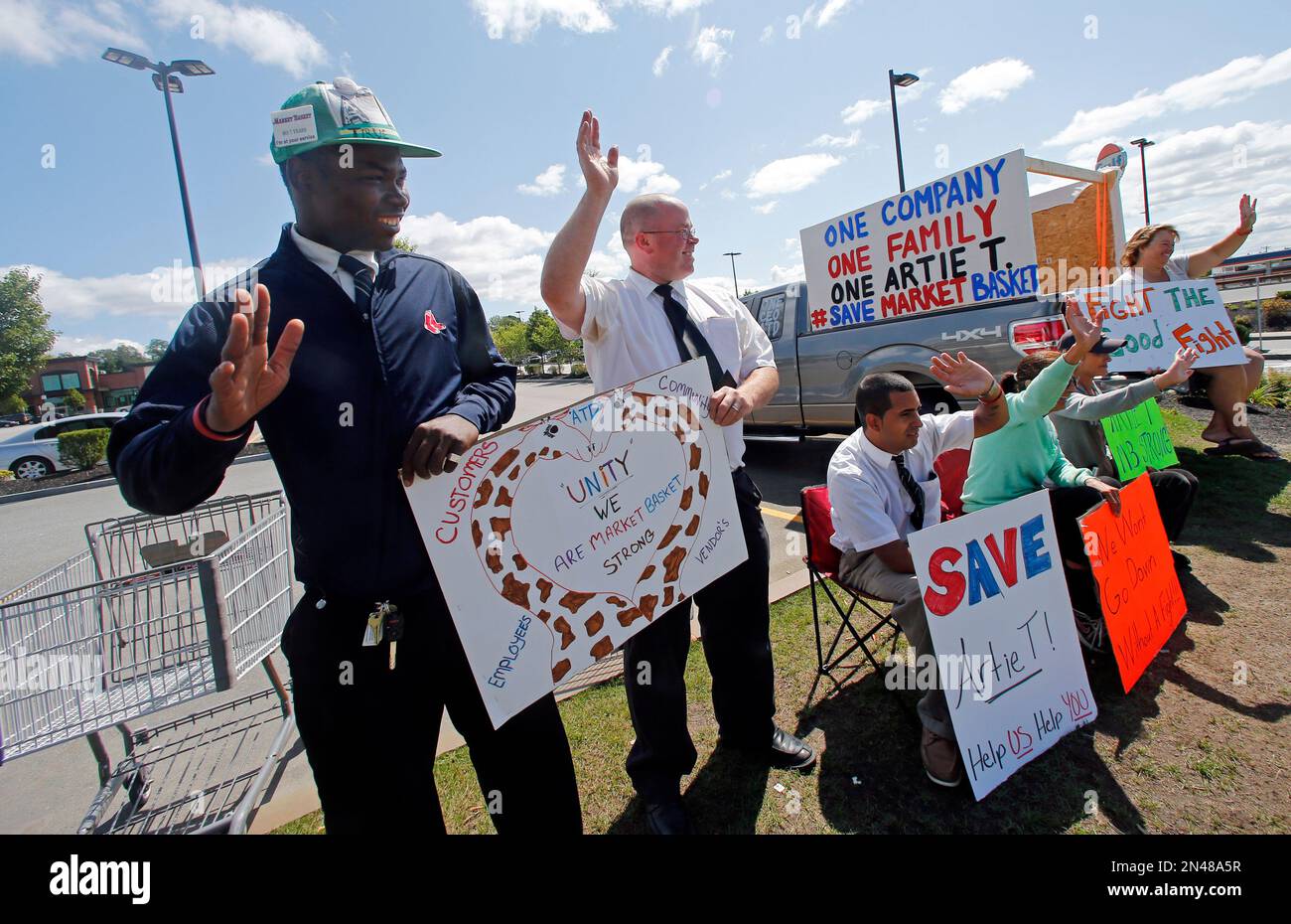 Market Basket employees hold signs and wave to passing supporters outside the supermarket in