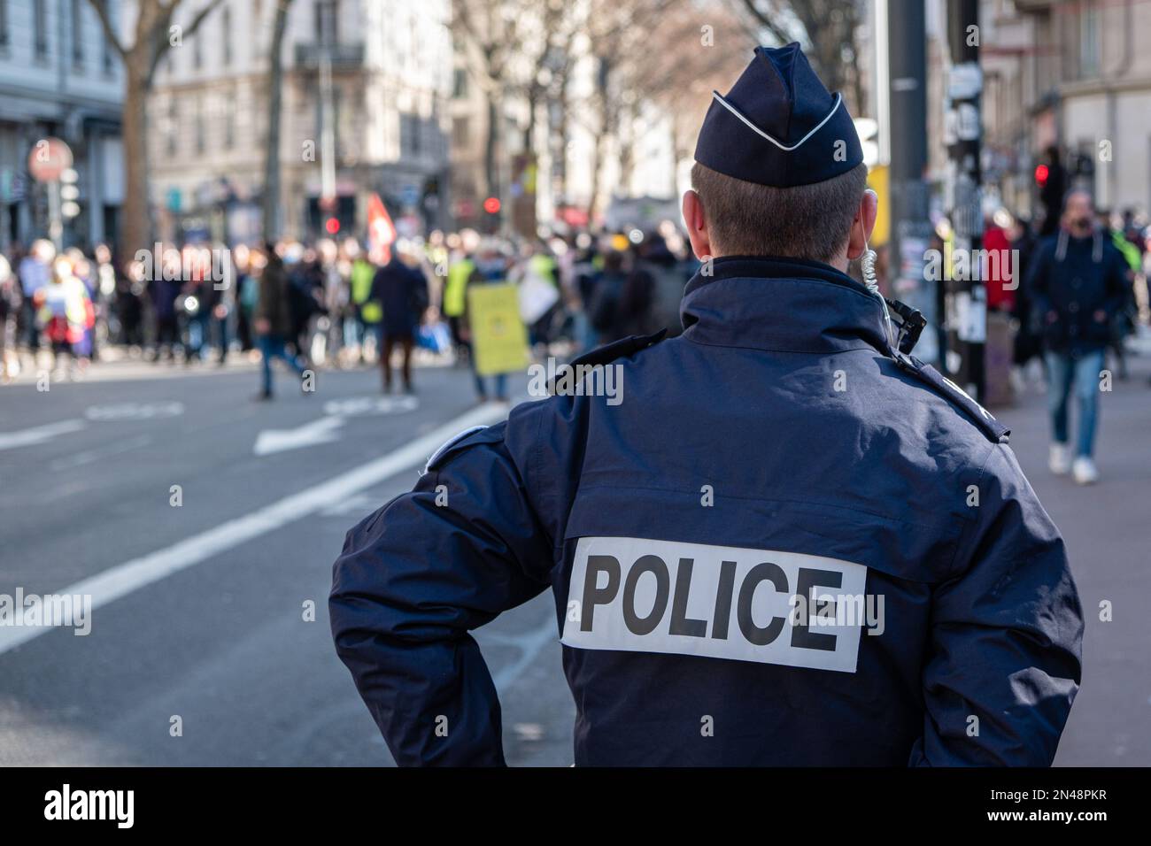France, Lyon, 2023-02-07. A policeman from behind watching the demonstrators in the march. Stock Photo