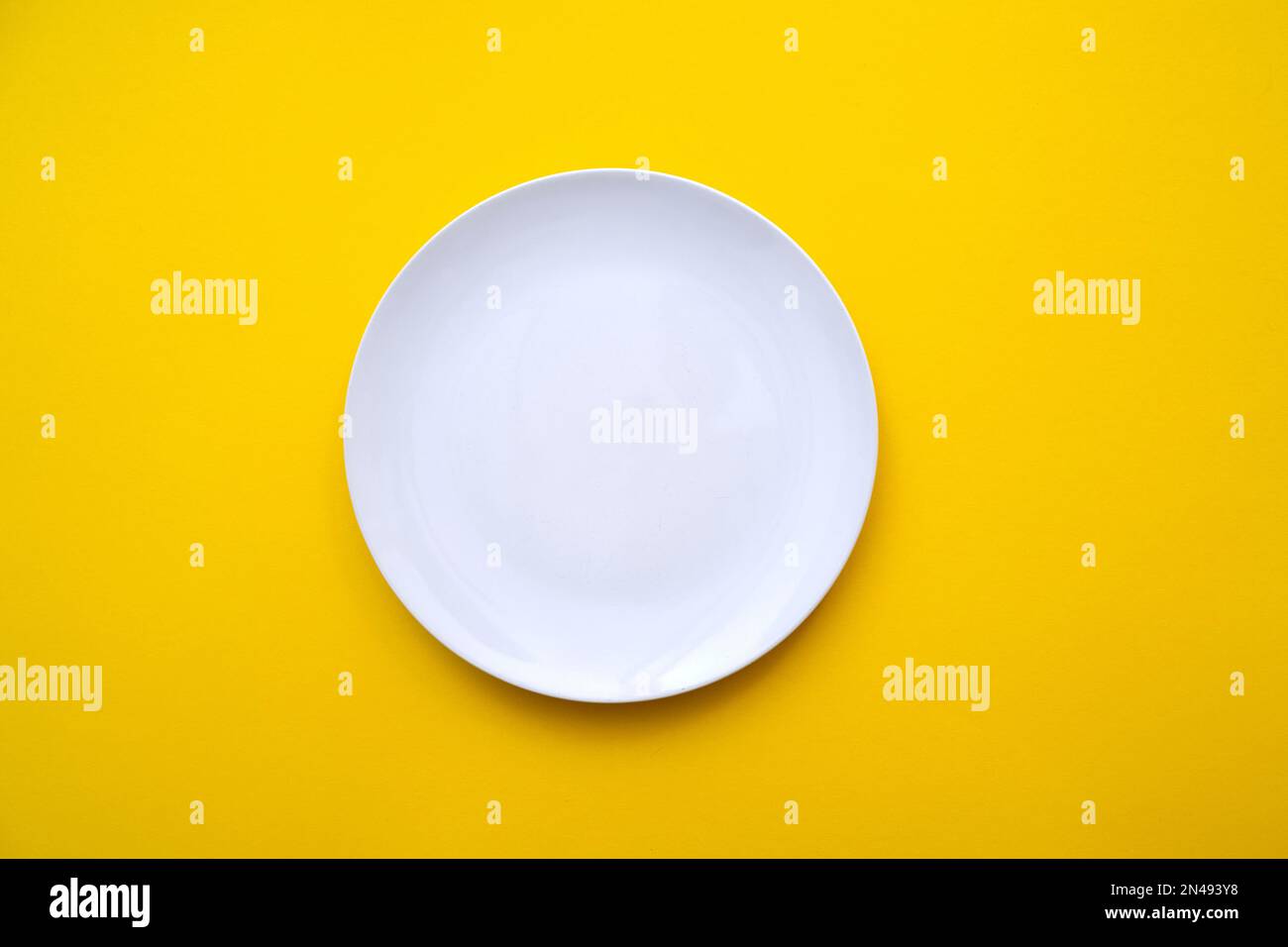 White empty plate with blank surface on bright yellow backdrop, top view Stock Photo