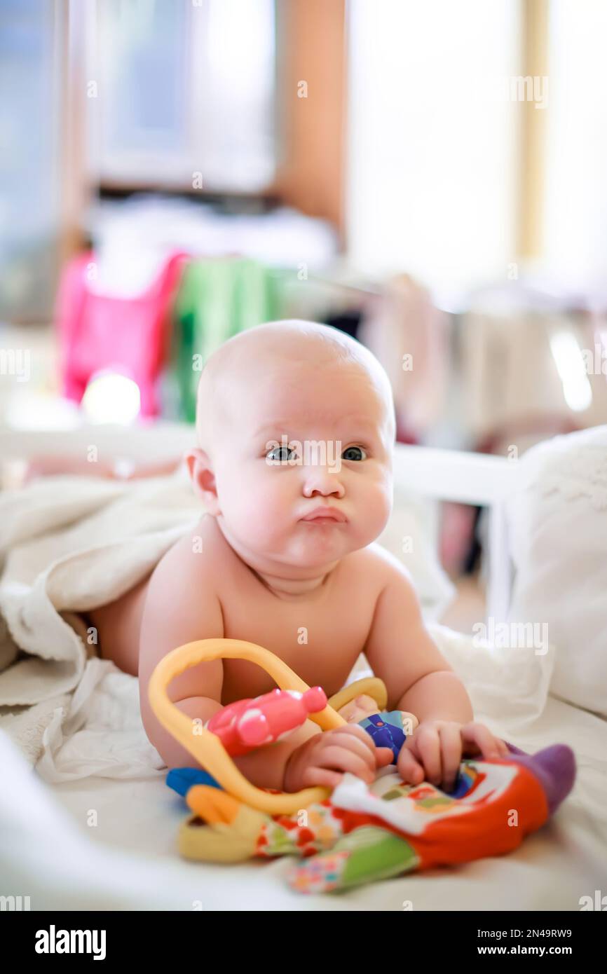 Funny kid in a crib. The kid puffed up his lips and tries to cry. A sad child in the background of the window. Stock Photo
