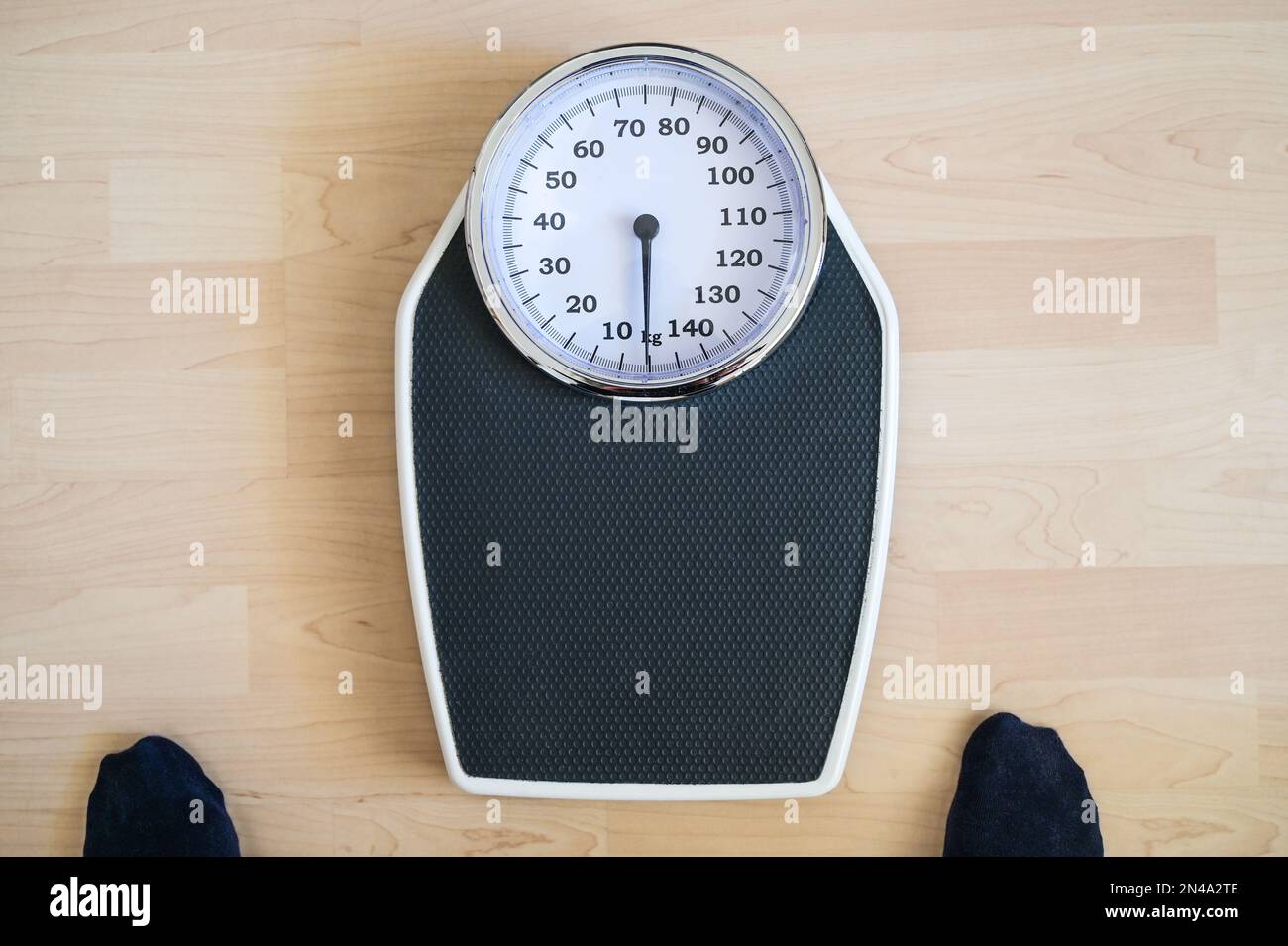 Analogue old-fashioned personal scale on a wooden floor, two feet in dark stockings hesitantly standing in front of it, worried about the weight, high Stock Photo