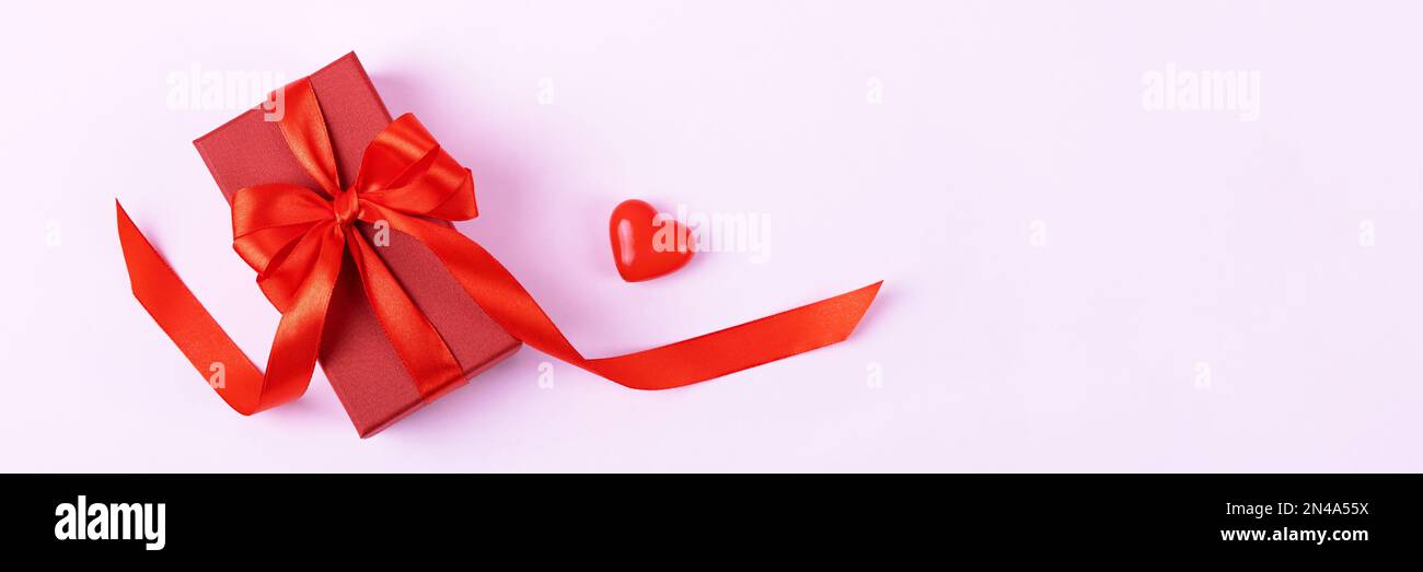A red gift box with a satin ribbon bow and a decorative heart. Festive ...