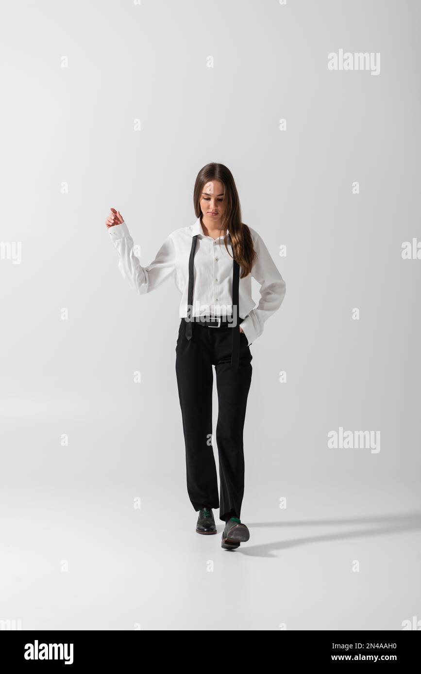 full length of brunette woman in black pants and suspenders walking ...