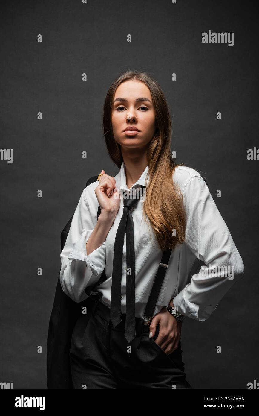 brunette woman with long hair standing in formal wear with suspenders ...