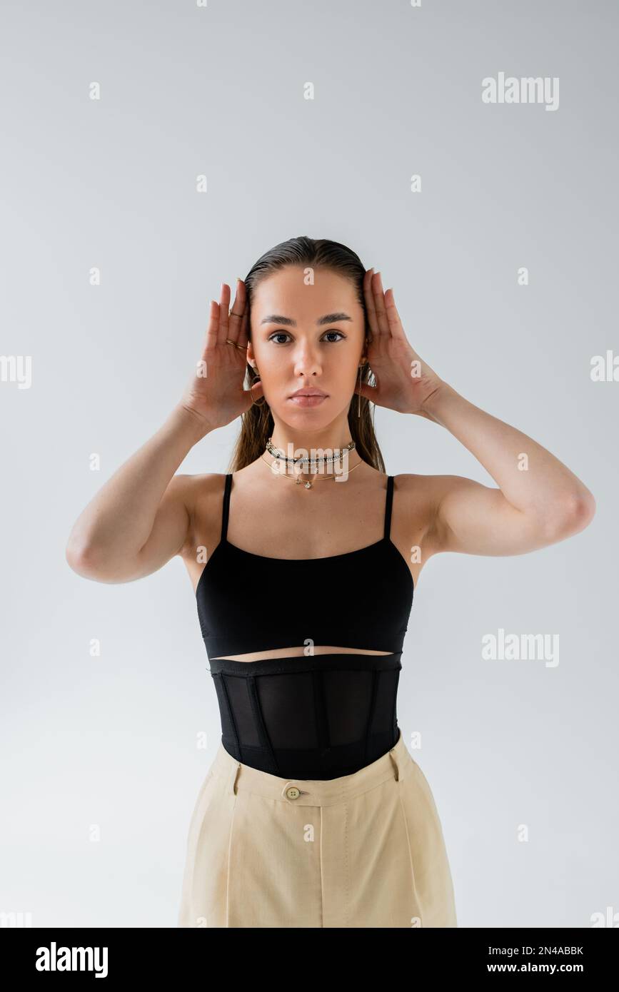 pretty model in beige pants and black top looking at camera while posing isolated on grey Stock Photo