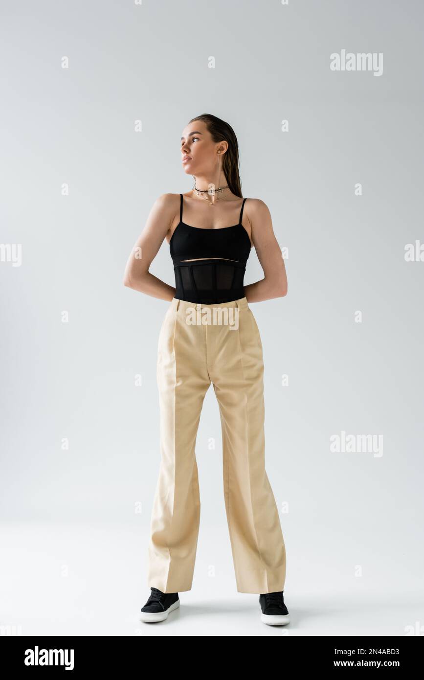 full length of pretty model in beige pants and black top looking away on grey Stock Photo