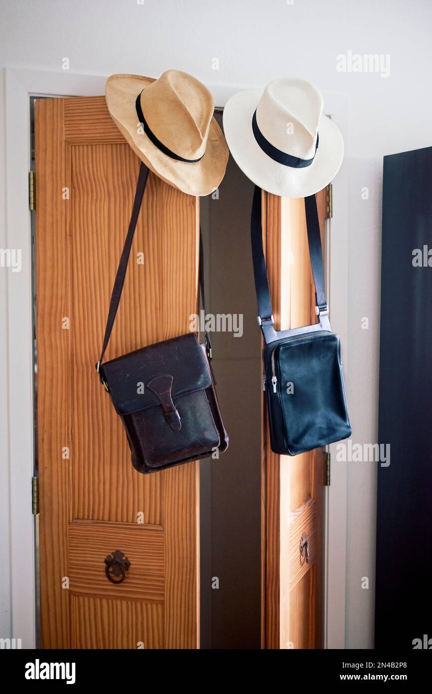 Vertical: His and hers straw hats and leather messenger-style bags hanging from French-style wooden doors Stock Photo