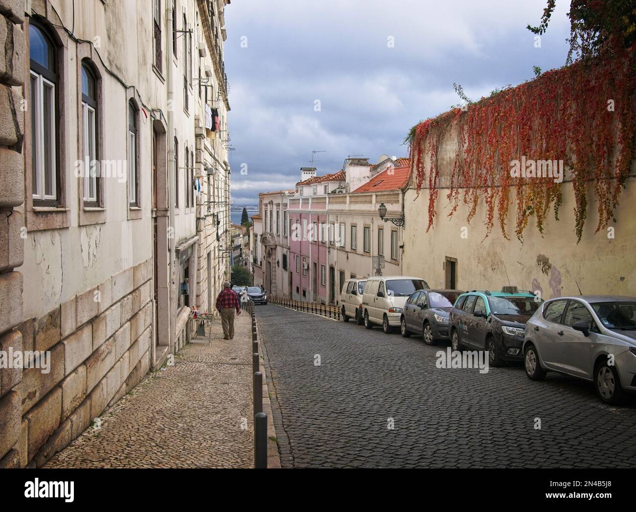 Narrow, curved, stone street on a hill descending to the Tagus River waterfront. Stock Photo