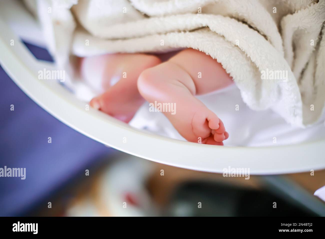 The legs of a newborn baby lying on the bed under a white blanket Stock