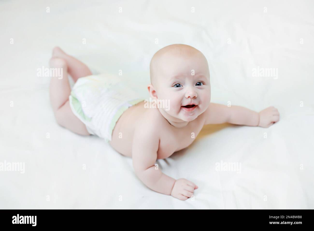 The baby lies on her tummy on the bed with her legs raised. Laying it