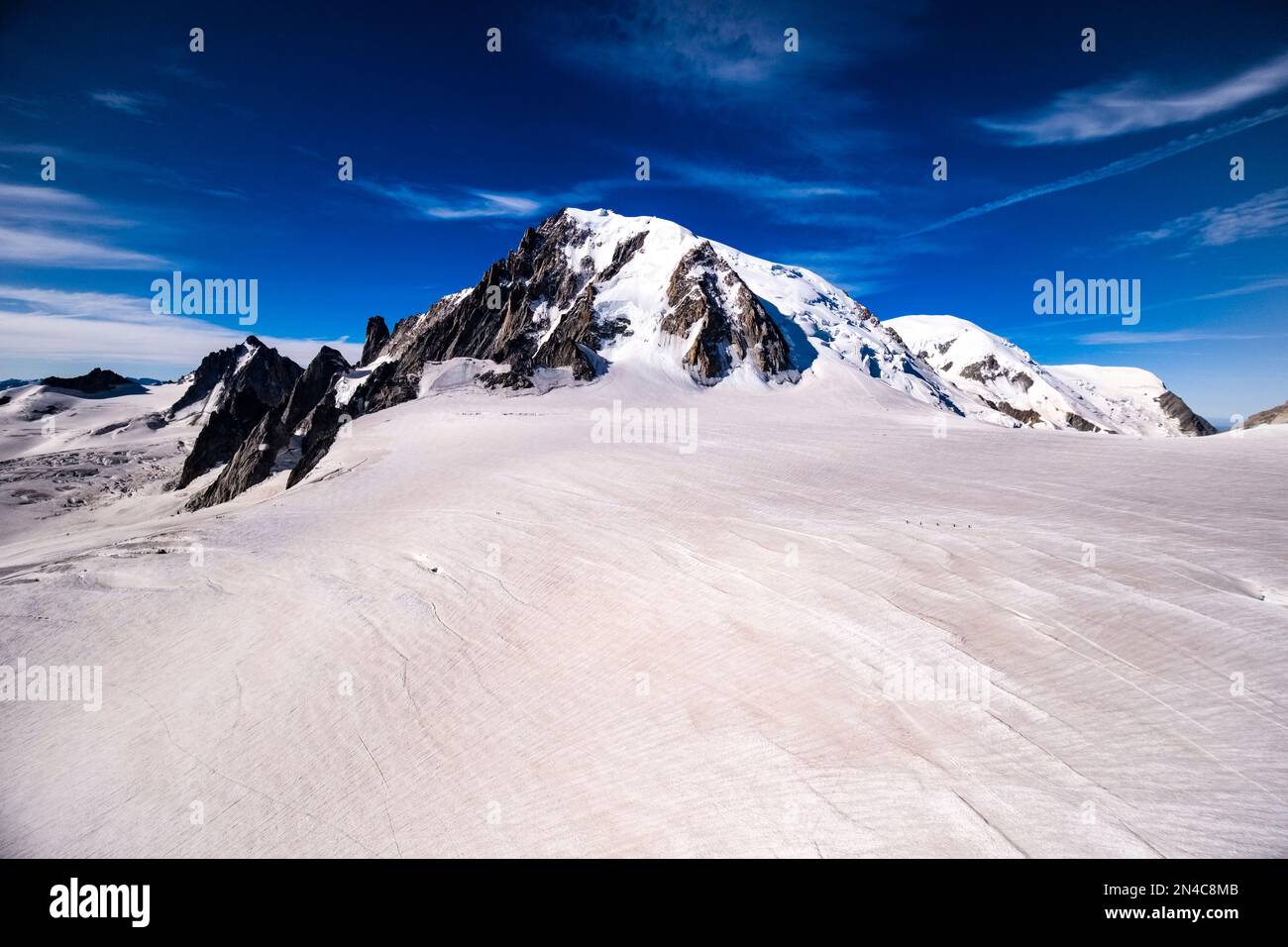 Alpinists crossing the upper part of the Géant Glacier, the summits of Mont Blanc du Tacul, Mont Blanc and Dome du Goutier in the distance. Stock Photo