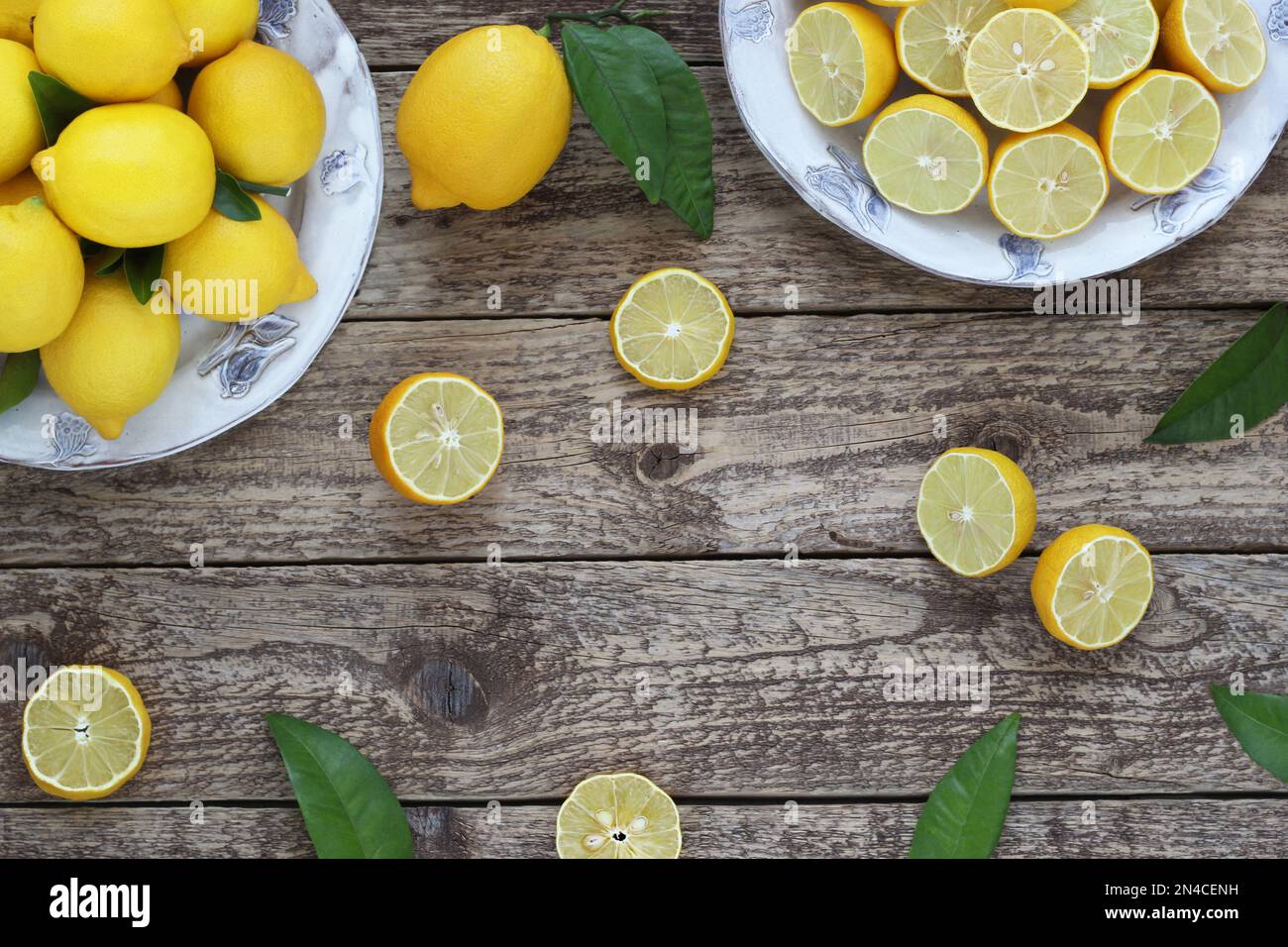Lemon citrus decorative frame or border on wooden background, arranged whole, halved and sliced lemon fruits on plates with leaves, table top view. Stock Photo