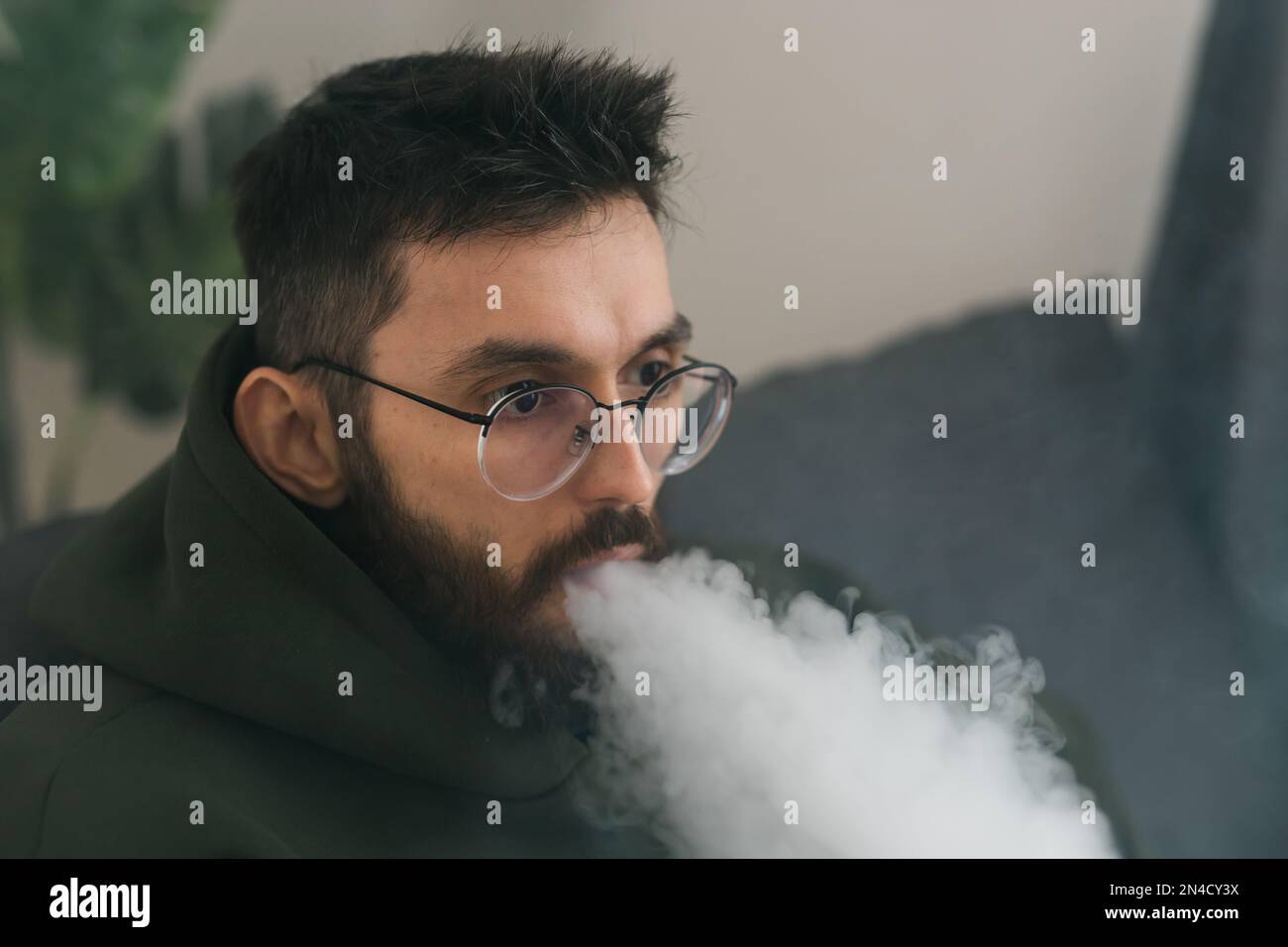 Bearded millennial or gen z man smoking hookah while relaxing on sofa