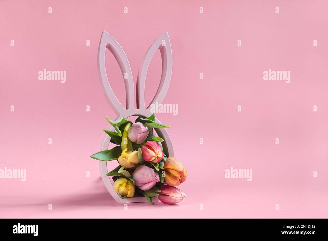 Wooden easter bunny statuette with spring tulips on the pink background, easter minimal concept with copy space Stock Photo