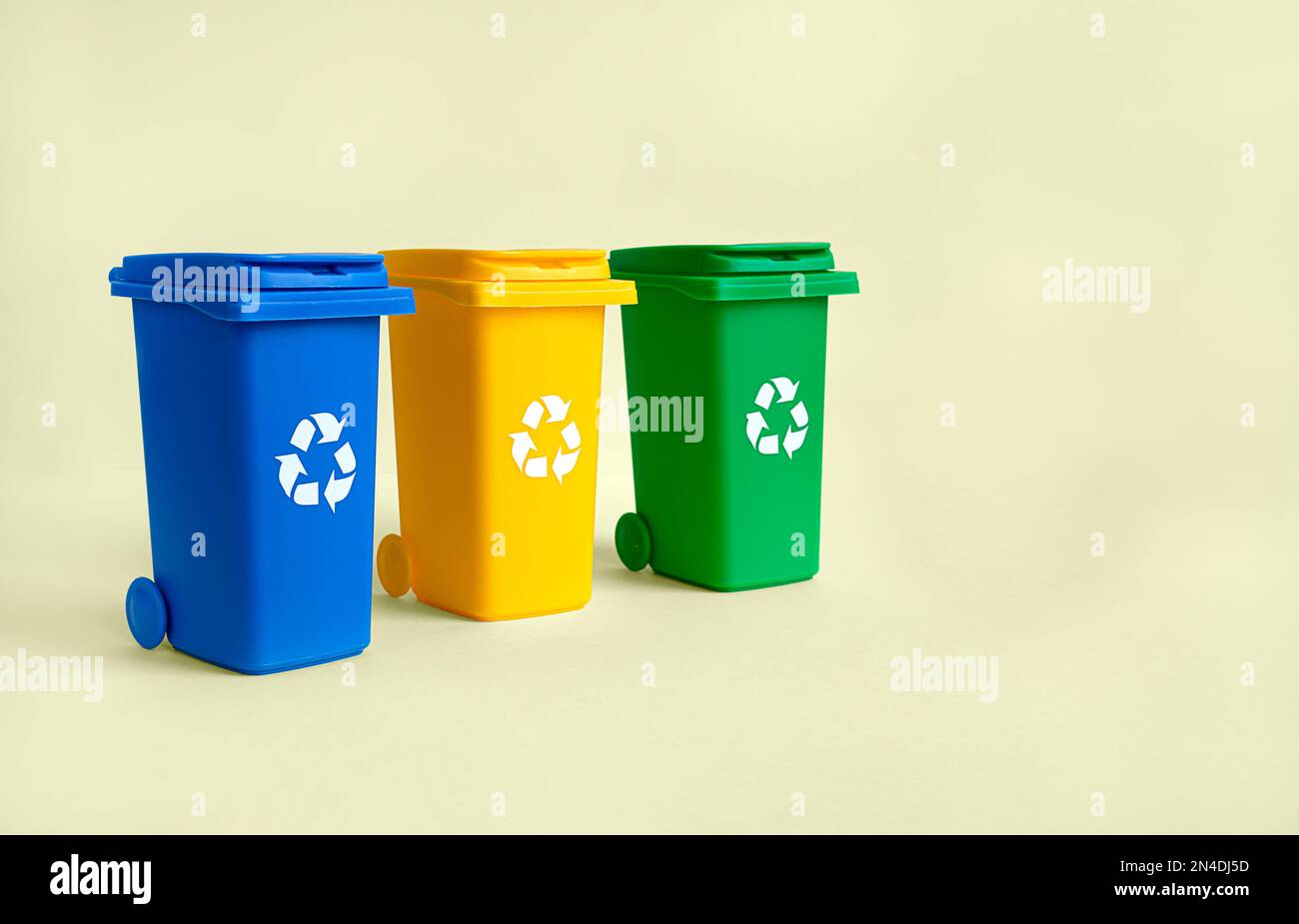 Blue, yellow and green container for separate plastic, paper and organics garbage collection, isolated on the yellow background with copy space, waste Stock Photo