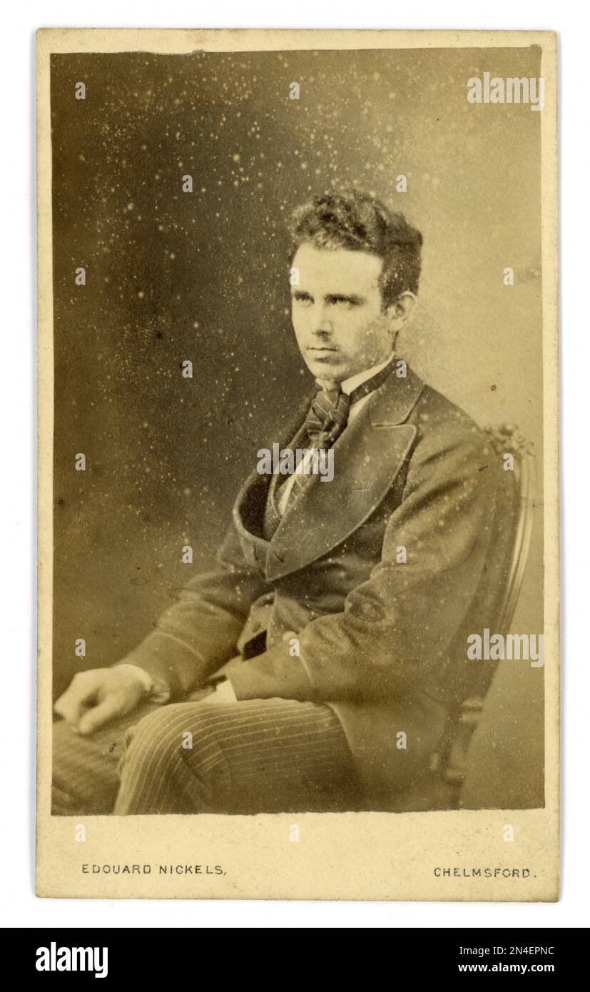 Original Victorian era CDV (carte de visite or visiting card) of scruffy, handsome, clean shaven young man, looking serious. He is wearing a loose-fitting 'sack' or lounge jacket with wide lapels, waistcoat and loose tie. Photograph from the studio of Edouard Nickels, Duke Street, Chelmsford, Essex, circa early 1870's Stock Photo