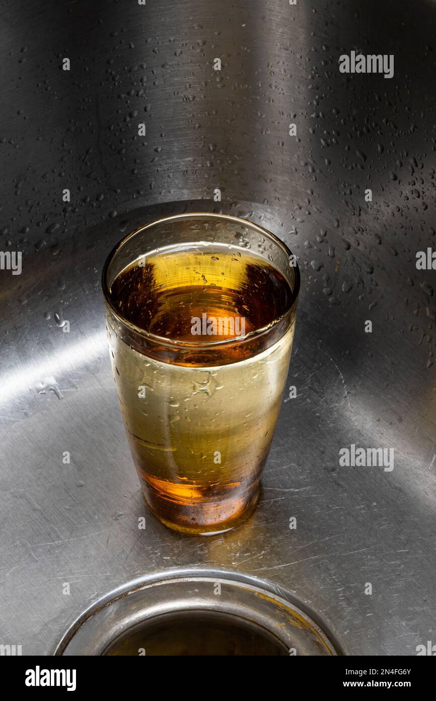 Gold colored drinking glass sitting in kitchen sink almost full of water. Stock Photo