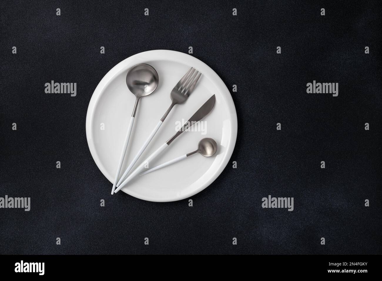 White plate and steel cutlery on a black grunge background. Top view. Card or menu template, flat design. Tableware, crockery. Aerial view, copy space Stock Photo