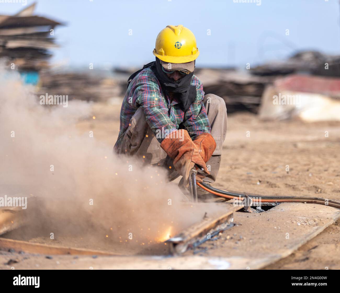 Gadani Pakistan August 2021, a worker wearing safety helmet cutting metal sheet with welding arc, labors working at ship bfreaking yard, labor day Pak Stock Photo