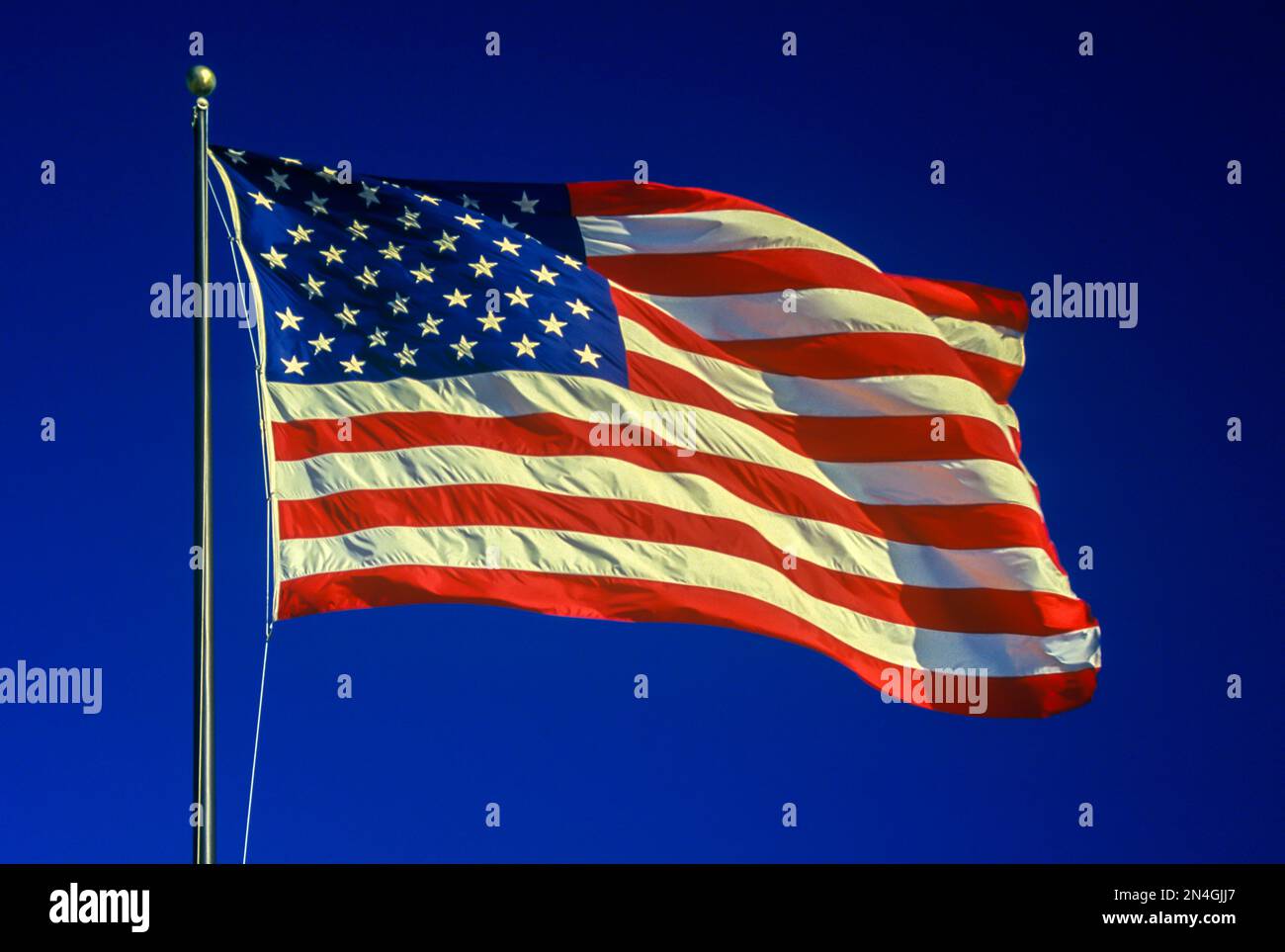 UNITED STATES FLAG FLYING ON FLAGPOLE WITH BLUE SKY Stock Photo