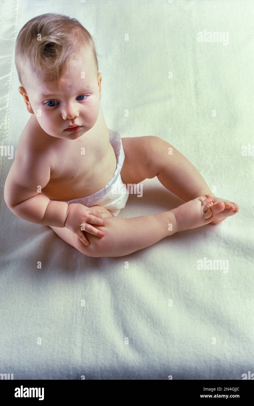 CAUCASIAN INFANT BABY SITTING UPRIGHT ON WHITE BLANKET Stock Photo