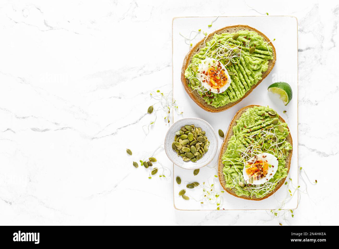 Avocado toast with boiled egg, seeds and sprouts on white background. Healthy diet food. Top view Stock Photo