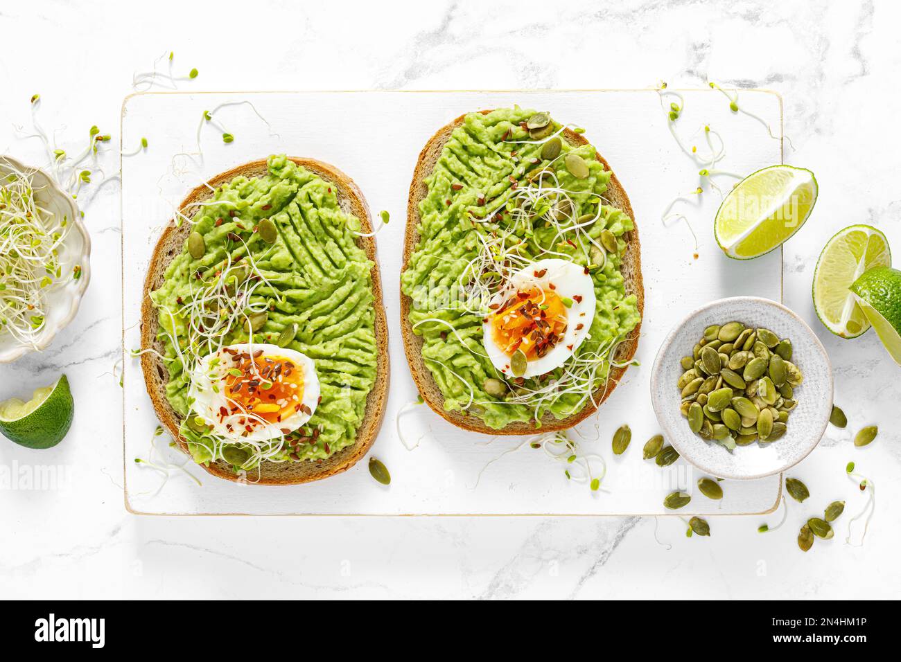 Avocado toast with boiled egg, seeds and sprouts on white background. Healthy diet food. Top view Stock Photo