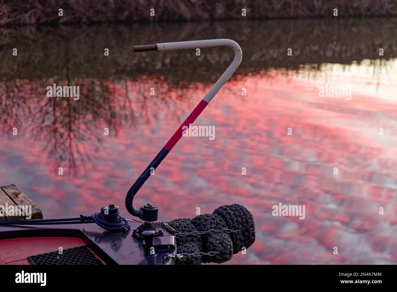 A narrowboat tiller in front of a reflection in the water of a sunset in the water behind Stock