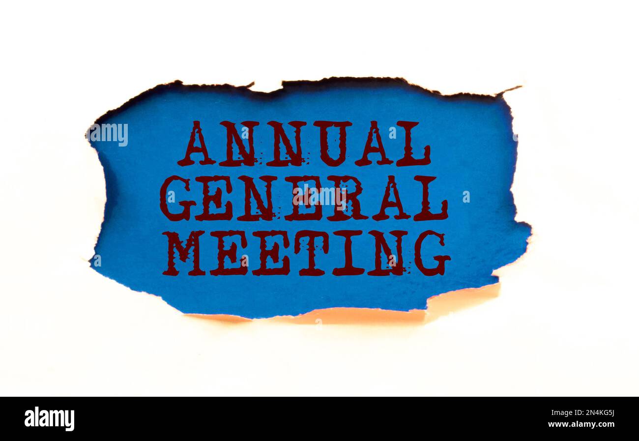On a light background, a white notebook with are words AGM Annual General Meeting and a pen. Stock Photo