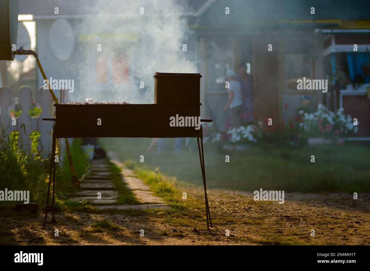 Iron grill with barbecue smokes in the rays of the setting sun on the