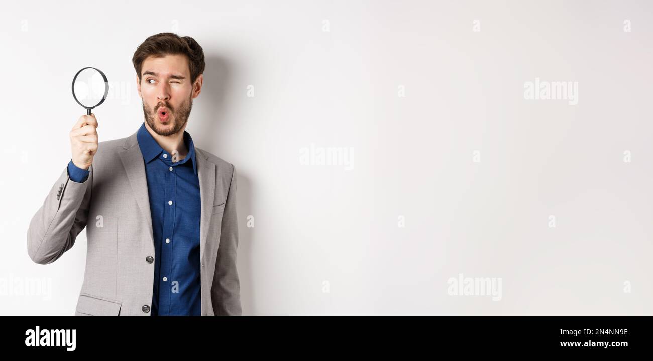 Excited funny guy in suit look through magnifying glass aside, checking