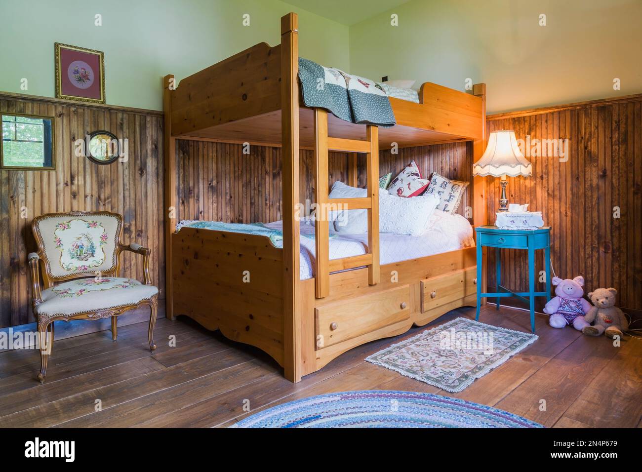 Child's bedroom with wooden bunkbed, antique upholstered armchair, turquoise nightstand on upstairs floor inside LEED certified country home. Stock Photo