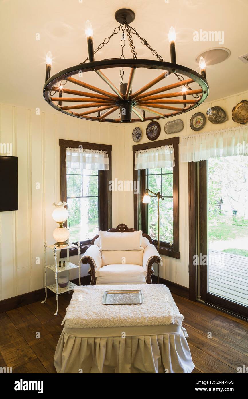 Study and reading room with white upholstered antique armchair and pleated fabric covered footstool, wagon wheel chandelier inside LEED certified home. Stock Photo