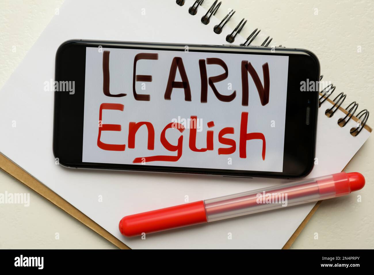 Smartphone with phrase Learn English, notepad and pen on white background, flat lay Stock Photo